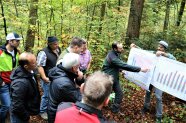 Ein Förster erklärt im Wald einer Gruppe von Menschen anhand von Plakaten eine Statistik.