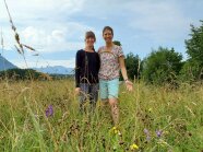Zwei Frauen stehen in einer Wiese, auf der Blumen blühen